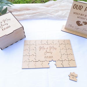 May include: Wooden wedding puzzle with a sign that reads "Our Puzzle Would Not Be Complete Without You. Please Sign a Piece." The puzzle is made of light brown wood and has a heart shape in the center. The sign is also made of light brown wood and has a heart shape in the center. The puzzle is a great way for guests to sign a wedding guest book.