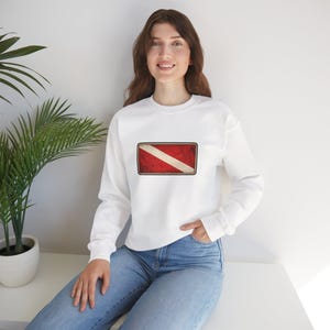 May include: White sweatshirt with a distressed dive flag design. The rectangular graphic features a diagonal white stripe across a red background, with a brown border. The long-sleeved sweatshirt is made of a soft material.