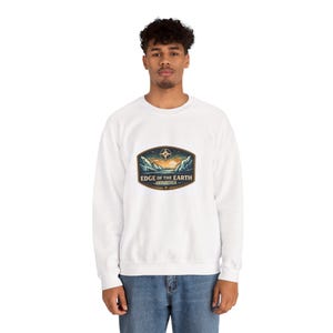 May include: White sweatshirt featuring a colorful graphic of a sunset over mountains with the text "EDGE OF THE EARTH - ANTARCTICA". The design includes a compass rose. The sweatshirt is a casual style.