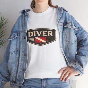 May include: White t-shirt with a distressed graphic that reads "DIVER" in a bold, vintage font. The graphic includes a red and white dive flag. The shirt is worn with a blue denim jacket.