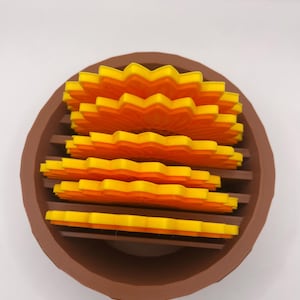 May include: A brown, circular decorative piece with horizontal slats, containing layers of yellow and orange, flower-shaped elements. The elements are arranged in tiers, forming a layered floral design.