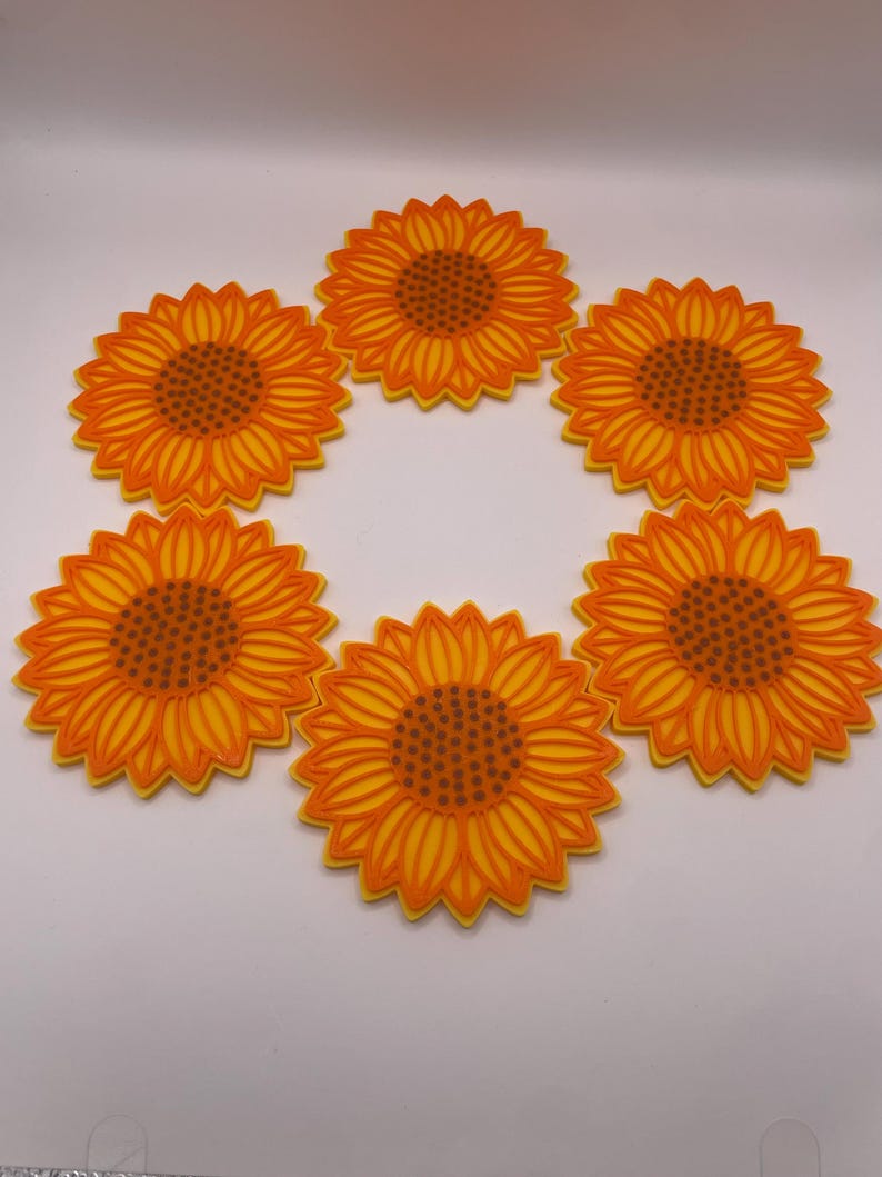 May include: Six sunflower-shaped coasters. Each coaster has a bright yellow and orange design, with a detailed centre and petal pattern. The coasters are arranged in a circular pattern, ideal for adding a touch of summer to any space.