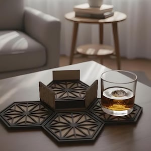 May include: A hexagonal coaster set with a geometric design, featuring a dark frame and a lighter interior. A glass of amber liquid with a large ice cube sits on one of the coasters. The coasters are arranged on a wooden table.