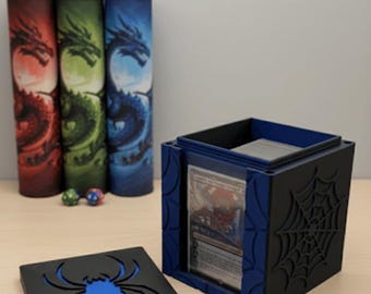 May include: A black and blue card storage box with a spiderweb design and a matching lid featuring a blue spider. Three cylindrical card holders with dragon illustrations in red, green, and blue are visible.