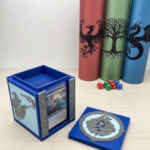 May include: A blue card storage box with a wizard design and a matching lid. Three cylindrical card mats in red, green, and blue, each with a different graphic. Dice in red, green, and blue are also visible.