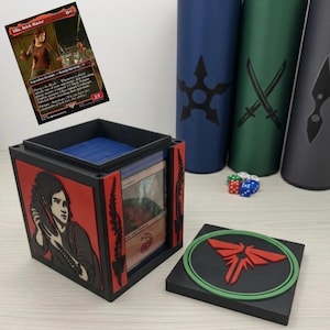 May include: A black and red gaming card deck box featuring a relief of a character on the side and a red firefly logo on the lid. The box contains a stack of cards and is displayed with a matching Ellie, Brick Master trading card and dice.