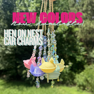 May include: A collection of hanging car charms featuring miniature hen-on-nest figures in pastel pink, purple, yellow, and blue. Each charm hangs from a gold-tone chain accented with clear and coloured beads. Text reads NEW COLORS Now Available! HEN ON NEST CAR CHARMS.