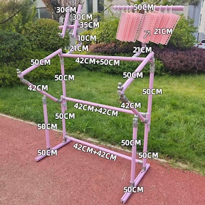 May include: A pink metal clothes drying rack with multiple horizontal bars and vertical supports. The rack has measurements labeled in centimeters, including 50 cm, 42 cm, and 30 cm sections. Several pink plastic hangers are attached to the top.