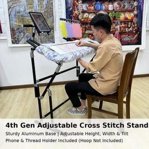 May include: A black adjustable cross stitch stand with a sturdy aluminum base. The stand includes a phone and thread holder. The text on the image reads: 4th Gen Adjustable Cross Stitch Stand. Adjustable height, width & tilt.