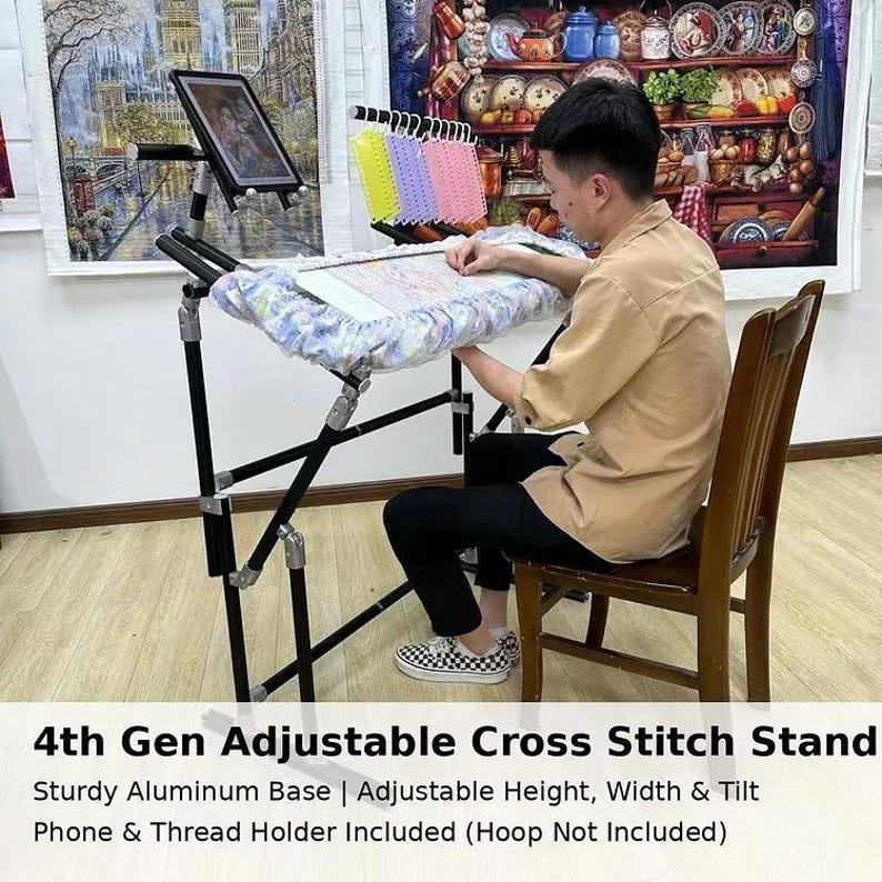 May include: A black adjustable cross stitch stand with a sturdy aluminum base. The stand includes a phone and thread holder. The text on the image reads: 4th Gen Adjustable Cross Stitch Stand. Adjustable height, width & tilt.