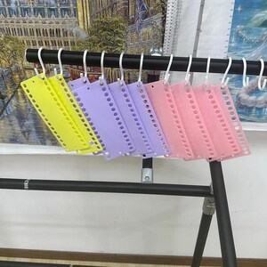 May include: A collection of colorful, plastic binder dividers hanging on a black metal rack. The dividers are yellow, purple, and pink, each with a series of holes along one edge for binding. White hooks suspend the dividers from the rack.