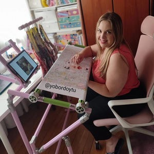 May include: A pink and silver cross-stitch frame with a tablet holder and a cross-stitch project in progress. The frame is adjustable and has a green bar. The text "@yobordoytu" is visible on the project.