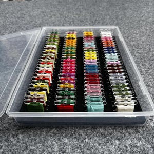 May include: A clear plastic organizer box filled with colorful embroidery floss. The floss is arranged in rows, showcasing a variety of colors including greens, yellows, reds, pinks, blues, and creams. The box is open, revealing the neatly organized spools.