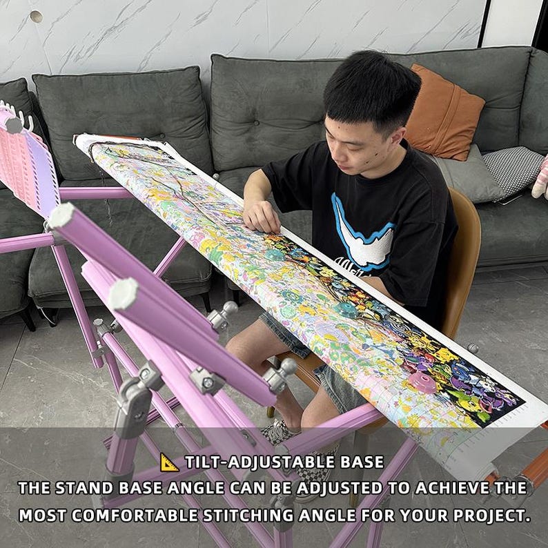 May include: A light purple, tilt-adjustable embroidery stand with a cross-stitch project in progress. The stand's base angle can be adjusted for comfortable stitching. The text on the image reads: "TILT-ADJUSTABLE BASE THE STAND BASE ANGLE CAN BE ADJUSTED TO ACHIEVE THE MOST COMFORTABLE STITCHING ANGLE FOR YOUR PROJECT."