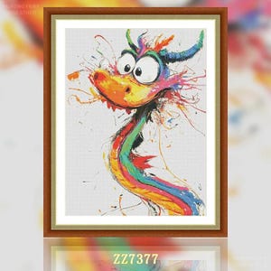 May include: A framed cross-stitch artwork featuring a whimsical dragon with a colorful, abstract design. The dragon has large, expressive eyes, an orange snout, and a rainbow-colored body. The artwork is set against a white background and framed in a brown wooden frame.