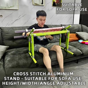 May include: A lime green cross stitch aluminium stand with adjustable height, width, and angle. The stand is designed for sofa use and features a cross stitch project in progress. Text on the image reads: "SUITABLE FOR SOFA USE" and "CROSS STITCH ALUMINUM STAND - SUITABLE FOR SOFA USE, HEIGHT/WIDTH/ANGLE ADJUSTABLE."