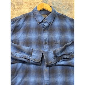 May include: A blue and gray plaid button-down shirt with long sleeves. The shirt has a button-down collar and a single chest pocket. The cuffs are buttoned. The shirt is made of a soft, woven fabric.