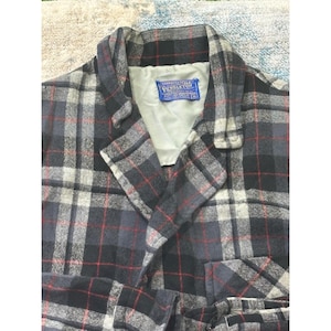 May include: A Pendleton wool jacket with a grey, black, and red plaid design. The jacket features a notched collar and a label that reads "Pendleton". The lining is a light beige colour.