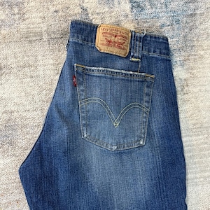 Puede incluir: Vaqueros azules de mezclilla con un diseño clásico de cinco bolsillos. Presentan un lavado descolorido, un bolsillo trasero con un diseño de costura amarilla y un parche de cuero con el logotipo de Levi Strauss & Co. Los vaqueros tienen un corte recto.