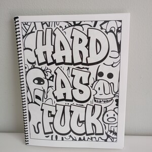May include: A white spiral-bound notebook with black and white doodle art. The cover features the words "HARD AS FUCK" in bold, stylized lettering. The artwork includes various cartoon characters and abstract designs.