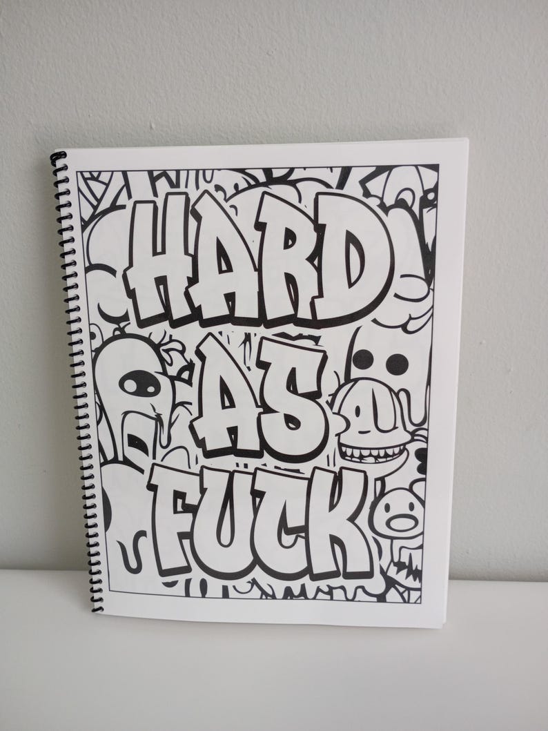 May include: A white spiral-bound notebook with black and white doodle art. The cover features the words "HARD AS FUCK" in bold, stylized lettering. The artwork includes various cartoon characters and abstract designs.