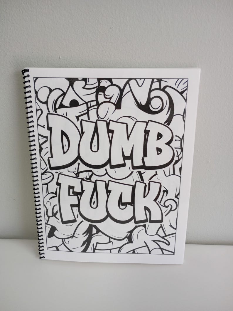 May include: A spiral-bound notebook with a black and white graffiti-style design. The words "DUMB FUCK" are prominently displayed in bold, bubble letters against a backdrop of abstract shapes and lines.
