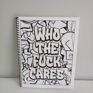 May include: A spiral-bound coloring book with a black and white graffiti design. The cover features the words "WHO THE FUCK CARES" in bold, stylized lettering. The background is filled with abstract graffiti elements.