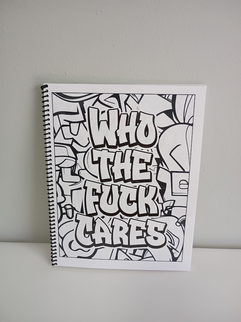 May include: A spiral-bound coloring book with a black and white graffiti design. The cover features the words "WHO THE FUCK CARES" in bold, stylized lettering. The background is filled with abstract graffiti elements.