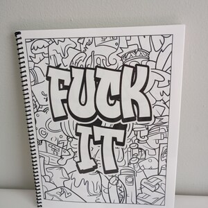 May include: A white spiral-bound coloring book with a black and white doodle design. The words "FUCK IT" are prominently displayed in bold, outlined letters. The background is filled with various cartoonish illustrations.