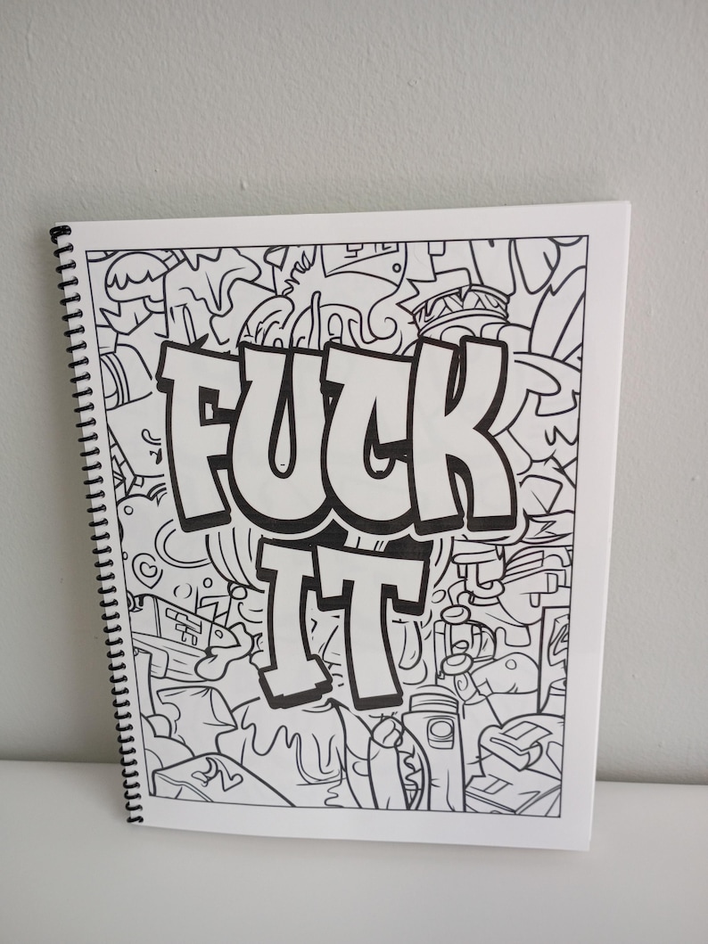 May include: A white spiral-bound coloring book with a black and white doodle design. The words "FUCK IT" are prominently displayed in bold, outlined letters. The background is filled with various cartoonish illustrations.