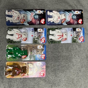 May include: Six Ty Beanie Babies in their original packaging. The Beanie Babies are all white with red accents and feature different country-themed designs. The packaging includes the names "Glory", "Maple", "Erin", and "Britannia".