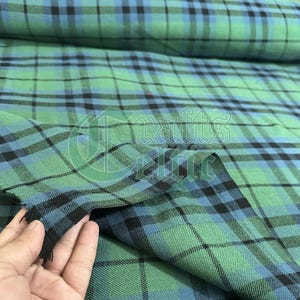 May include: Close-up of a green, blue, and black plaid fabric. The fabric has a woven texture with a repeating pattern of intersecting lines. The colors are vibrant, with a mix of light and dark shades. The fabric is likely used for clothing or home decor.