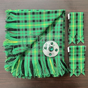 May include: A green, black, and yellow plaid kilt with a fringe border. The kilt is folded in half and a silver kilt pin with green stones is on top. Two matching green, black, and yellow plaid kilt hose are on the right side of the image.