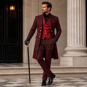 Op de afbeelding: Een lang gesneden zwart-rood gestreepte blazer, gecombineerd met een bijpassende gestreepte broek en een effen rood vest. Het ensemble is voorzien van goudkleurige knopen, een zwart overhemd, een zwarte vlinderdas, zwarte leren handschoenen en een zwarte wandelstok.
