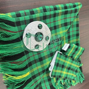 May include: A green, black, and yellow plaid kilt with a silver kilt pin featuring green gemstones. The kilt has a fringe around the bottom.