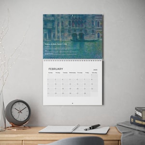 May include: A wall calendar for February 2025, featuring a painting of a Venetian scene. The artwork is predominantly blue and green, with a gondola visible. The calendar is hanging on a gray wall, with a clock and desk visible.