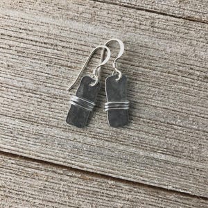 May include: A pair of silver earrings with a rectangular, hammered metal design. The rectangular shape is wrapped with silver wire. The earrings have a simple hook closure.