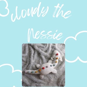 Könnte beinhalten: Ein weißes, gehäkeltes Nessie-Plüschtier mit bunten Punkten auf dem Rücken. Das Spielzeug liegt auf einer flauschigen weißen Decke. Der Text "Cloudy the Nessie" ist in Weiß auf hellblauem Hintergrund geschrieben.