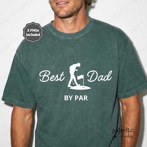 Puede incluir: Una camiseta de color verde oscuro con efecto lavado mineral que presenta un texto blanco impreso que dice Best Dad BY PAR, junto a un gráfico de un golfista en un green con una bandera. La prenda tiene cuello redondo y mangas cortas.