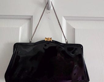 Bolsa de mão vintage em couro envernizado preto, estilo carteira de noite, com corrente dourada e fecho de laço.