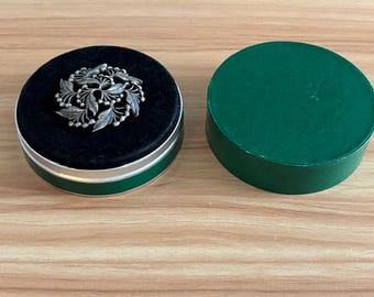 Broche redondo de peltre con diseño de hojas de acebo y bayas de Amway, año 1973, en su caja original.