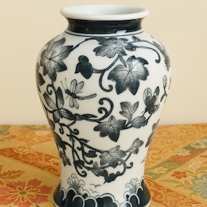 Op de afbeelding: Vintage Japanse porseleinen vaas met een witte body en donkerblauw bloemmotief. De vaas heeft een uitlopende voet, een smalle hals en een brede rand. De tekst "VINTAGE JAPANESE PORCELAIN VASE" staat bovenaan de afbeelding.