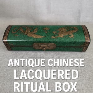 Puede incluir: Antigua caja ritual lacada china. La caja es de color verde oscuro con diseños dorados de dragones y fénix. La caja tiene un cierre de latón y adornos decorativos. El texto de la caja dice "ANTIQUE CHINESE LACQUERED RITUAL BOX."