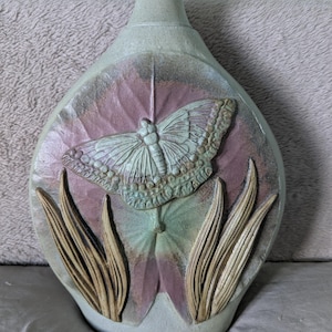 Puede incluir: Una taza de cerámica blanca con un asa negra y el texto "But First, Coffee" en negrita negra. La taza se encuentra sobre un fondo borroso, sugiriendo un ambiente acogedor.