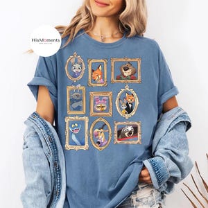 Puede incluir: Camiseta azul con retratos enmarcados de personajes de la pel&iacute;cula animada Zootr&oacute;polis. Los retratos est&aacute;n en marcos dorados e incluyen a Judy Hopps y Nick Wilde. La camiseta tiene el texto "HisMoments" en la parte superior izquierda.