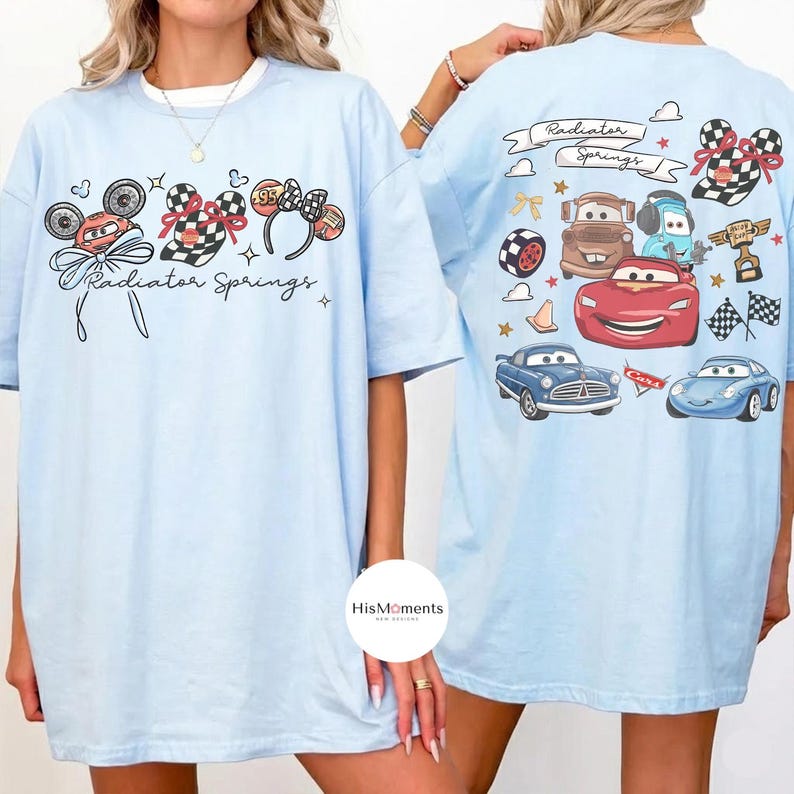Może przedstawiać: Jasnoniebieskie koszulki z grafiką z przodu i z tyłu. Z przodu znajdują się uszy Myszki Miki, kraciasta kokarda i napis "Radiator Springs". Z tyłu znajdują się kresk&oacute;wkowe samochody i napis "Radiator Springs."