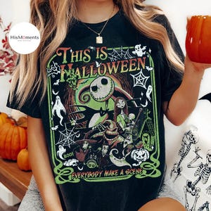 K&ouml;nnte beinhalten: Schwarzes T-Shirt mit einem farbenfrohen Grafikdesign aus "The Nightmare Before Christmas". Das Design zeigt Jack Skellington, Sally und andere Charaktere mit dem Text "This Is Halloween" und "Everybody Make a Scene" in Gr&uuml;n und Rot. Das Shirt hat einen Vintage-Look.