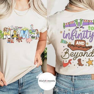 May include: Cream-coloured t-shirt with a colourful design featuring the word "NAME" and cartoon characters. The back of the shirt displays the phrase "to infinity and beyond" with related graphics. The shirt is made of a soft material.