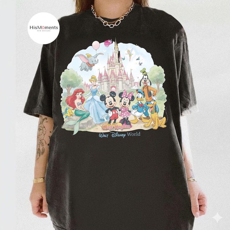 Pu&ograve; includere: Una t-shirt nera con una grafica colorata di vari personaggi dei cartoni animati davanti a un castello. La stampa include Topolino, Minnie, Paperino, Pippo, Pluto, Ariel, Cenerentola e Dumbo, con il testo Magic Kingdom Walt Disney World.