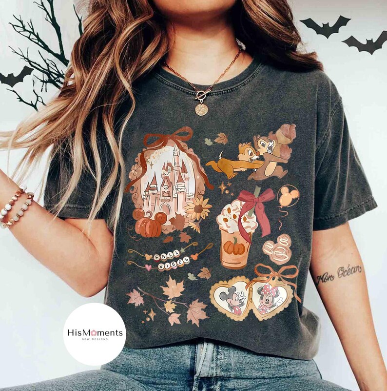 Op de afbeelding: Donkergrijs T-shirt met een herfstthema. Het ontwerp bevat een kasteel, pompoenen, Chip en Dale, een pumpkin spice latte en Mickey en Minnie Mouse. De woorden "Good Vibes" zijn ook aanwezig.